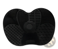 Black silicone heart shaped grooming mat with textured surfaces and central circular button for makeup brush cleaning