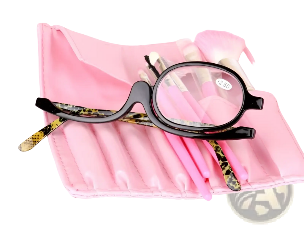 Black-framed makeup reading glasses with leopard-print temple tips resting on a pink makeup brush roll with +2.50 strength
