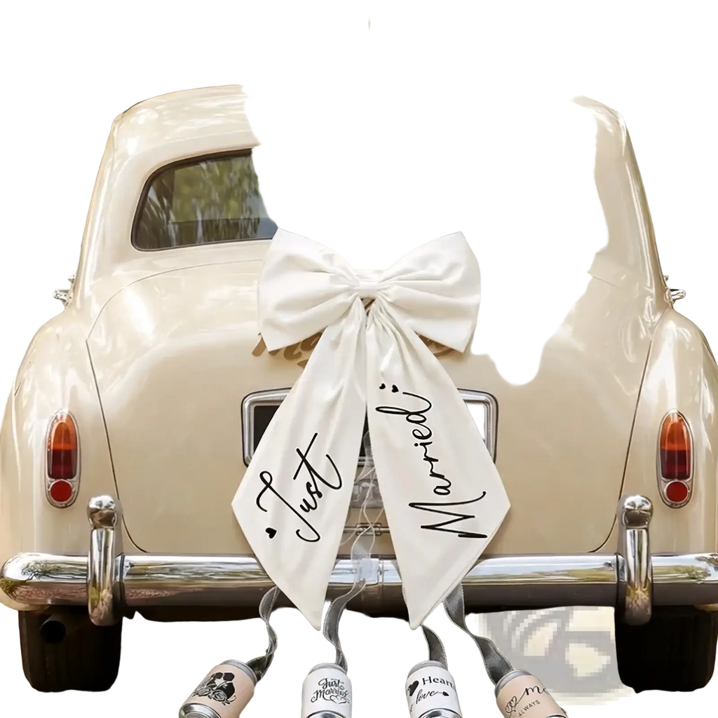 A cream-colored vintage car with a large white satin just married car bow wedding decor in elegant black cursive