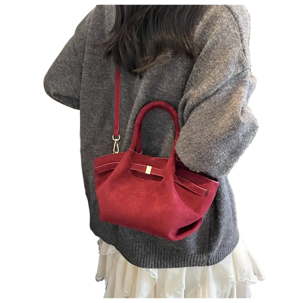 A plush red suede crossbody bag with structured top handle gold-tone hardware and adjustable shoulder strap