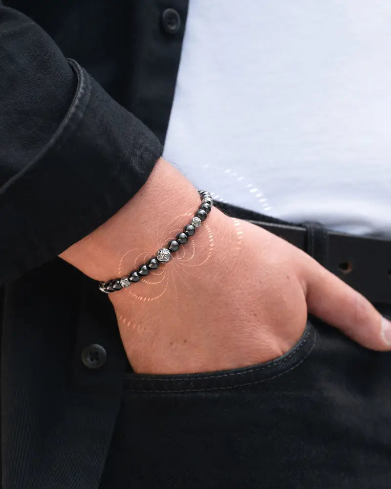 A sleek black beaded magnetic hematite skull bracelet with a silver-toned accent worn on the wrist