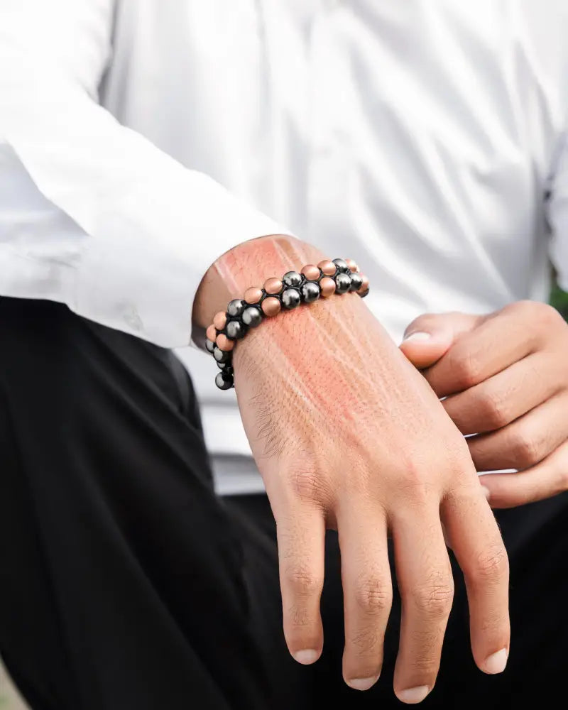 A two-strand magnetic hematite and copper bracelet with alternating black and peach beads worn on a wrist