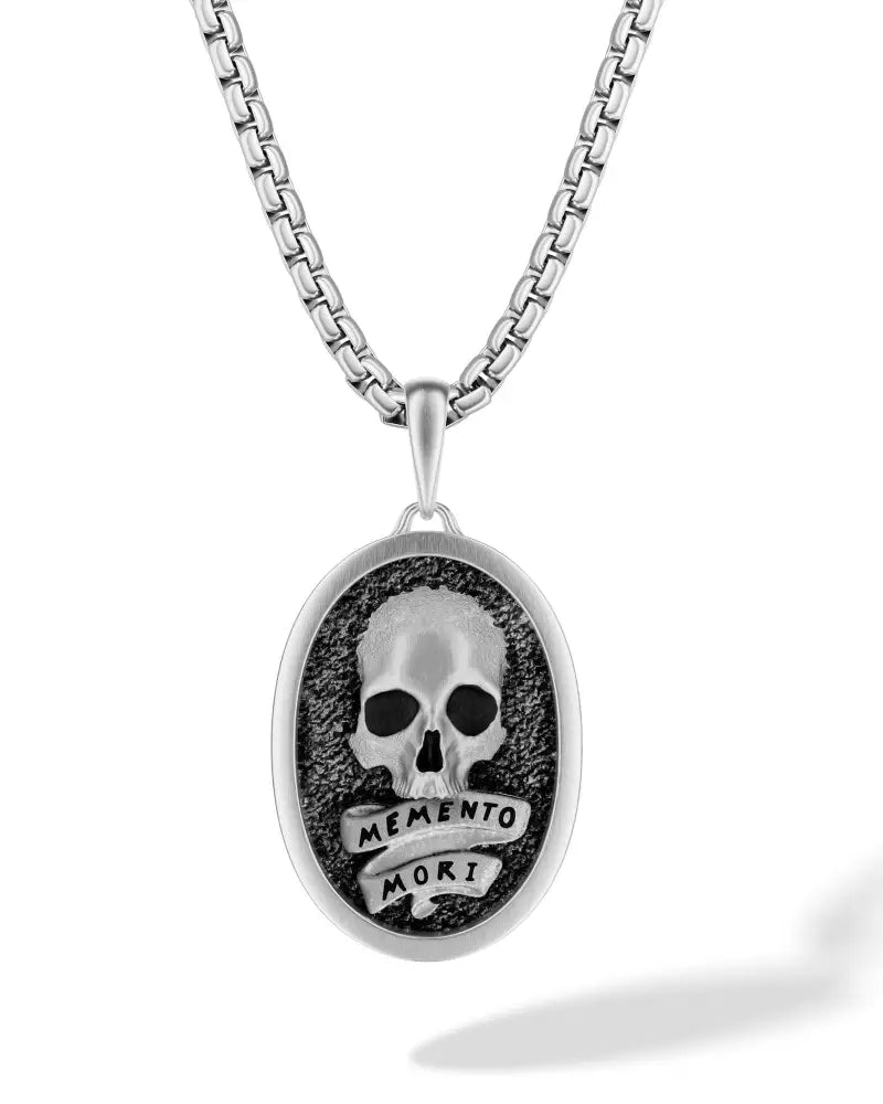 Silver stainless steel oval pendant necklace with detailed skull design and memento mori inscription on black background