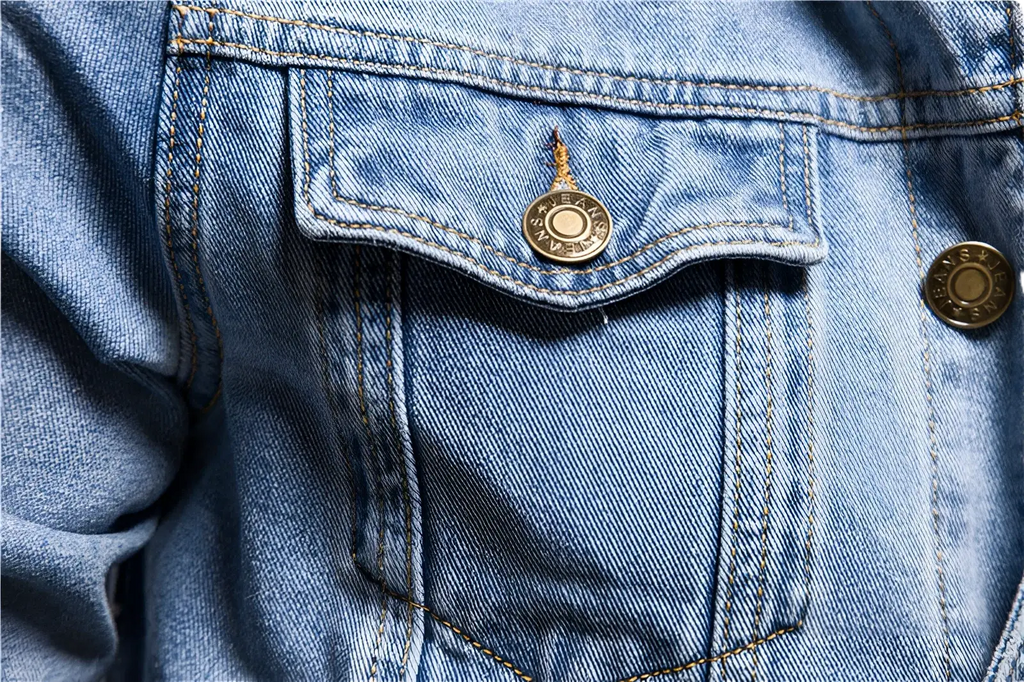 A gold-toned circular button with engraved text on the pocket of a men light wash slim fit denim jacket