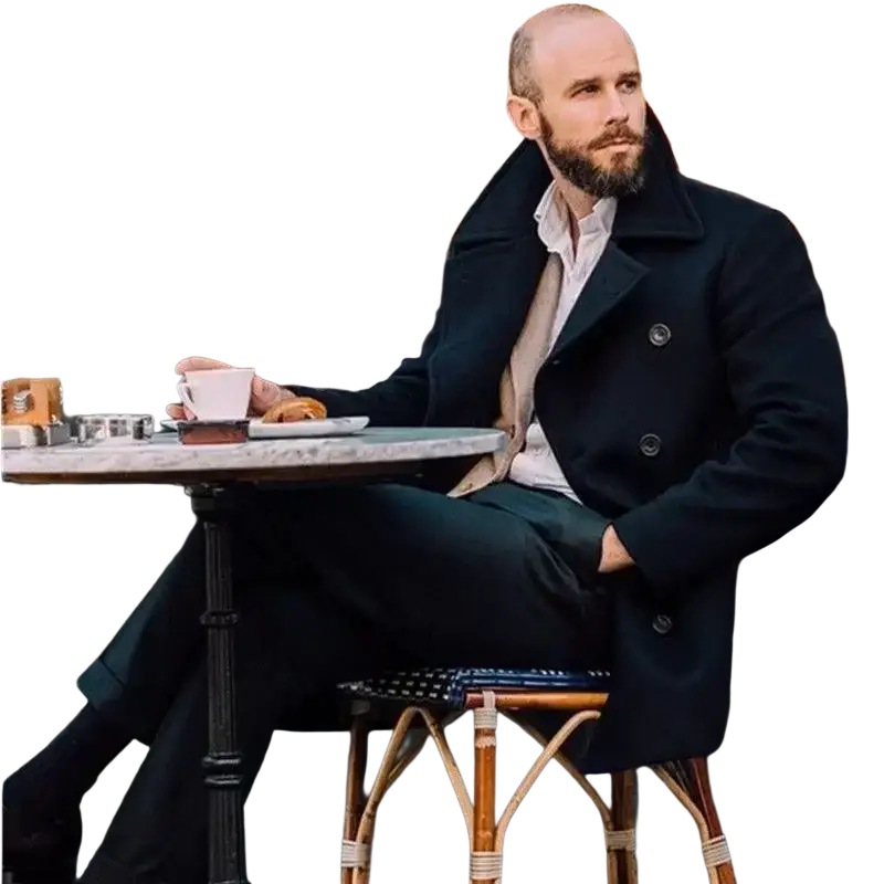 A man wearing a dark navy double-breasted wool peacoat sits at an outdoor café table in winter