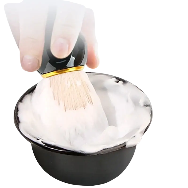 Black shaving brush with gold trim and light bristles dipped into white lather in wet shaving bowl kit