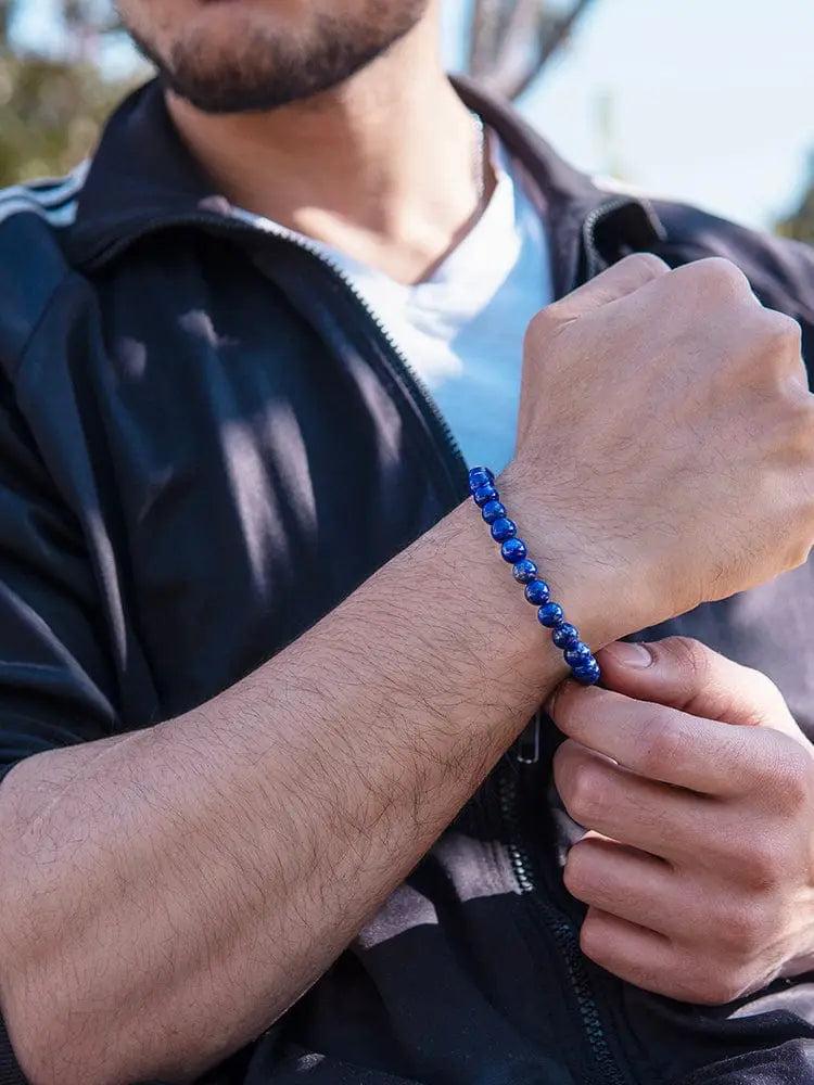 A vibrant royal blue lapis lazuli beaded bracelet with silver clasp worn on a man’s wrist with a polished finish