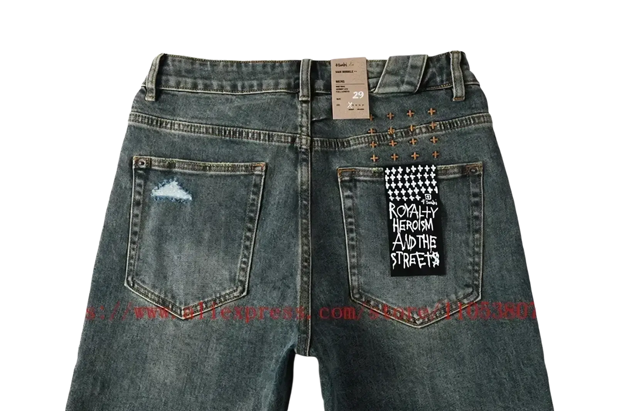 Back side of men’s distressed blue acid wash denim shorts with a cloud-like tear, metallic studs, and black patch detailing