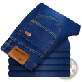 A stack of men’s slim fit stretch denim jeans in dark blue with brown leather brand tags and contrasting stitching