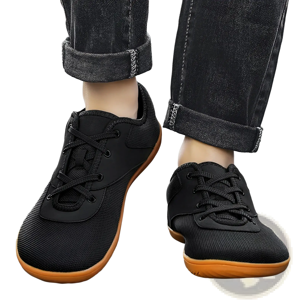Men’s wide toe breathable mesh running sneakers in black with orange rubber soles and black laces shown from the back
