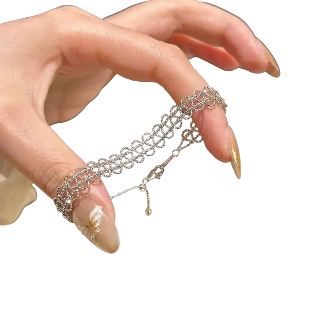 A delicate silver metal lace bracelet with an intricate pattern and an adjustable small dangling charm
