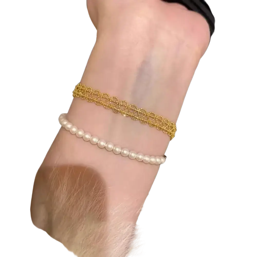 Metal lace bracelet in gold with intricate lace-like design worn alongside white pearl strand fashion jewelry