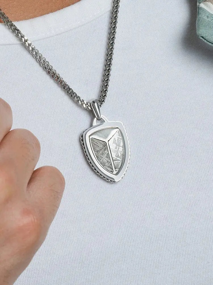 Silver shield-shaped pendant with textured metallic surface and embedded muonionalusta meteorite fragment on wheat chain
