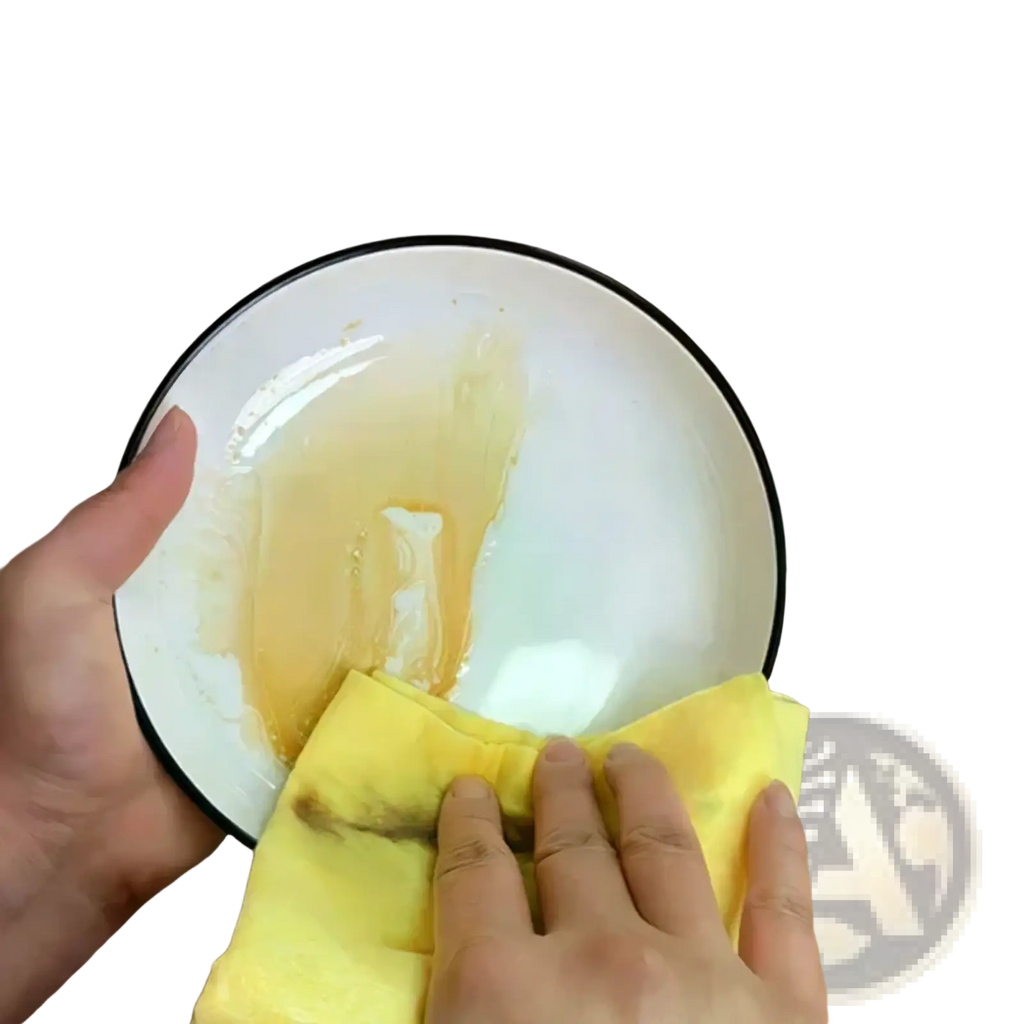 Yellow microfiber kitchen dishcloth wiping clean a white plate with black rim showing reusable cleaning towels