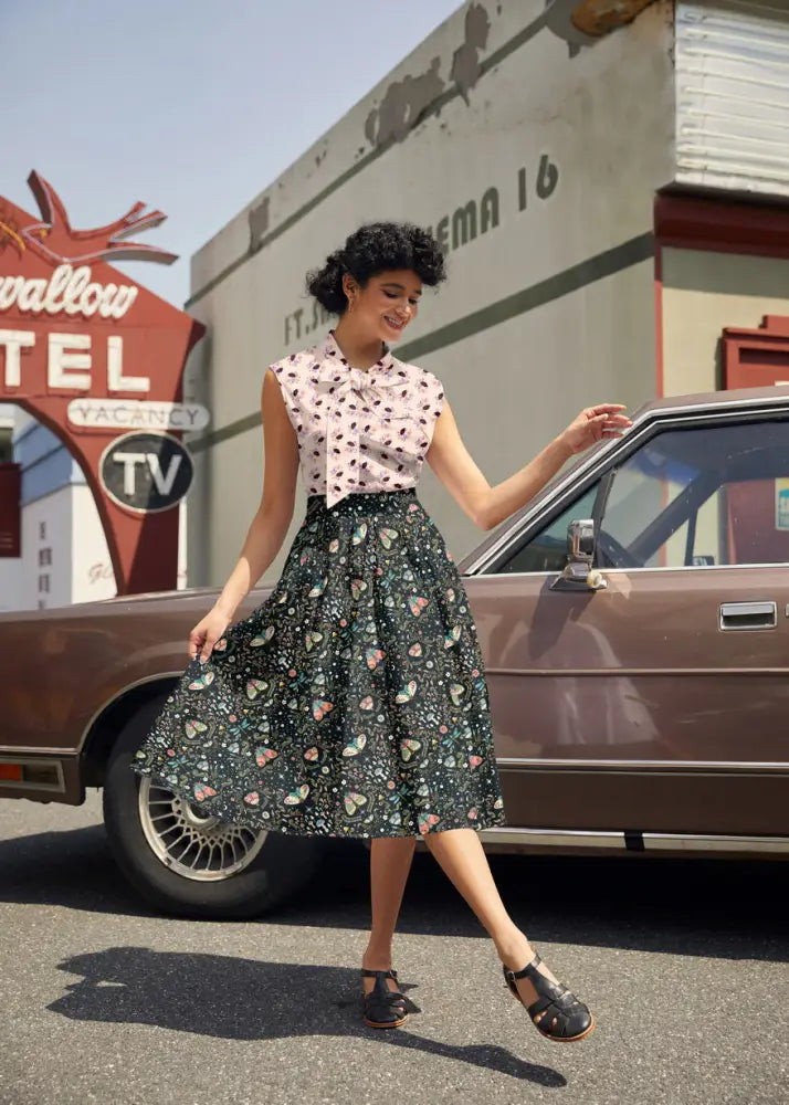 A woman wearing a vintage-style midnight Doris black pleated floral skirt with pink heart patterns and matching blouse