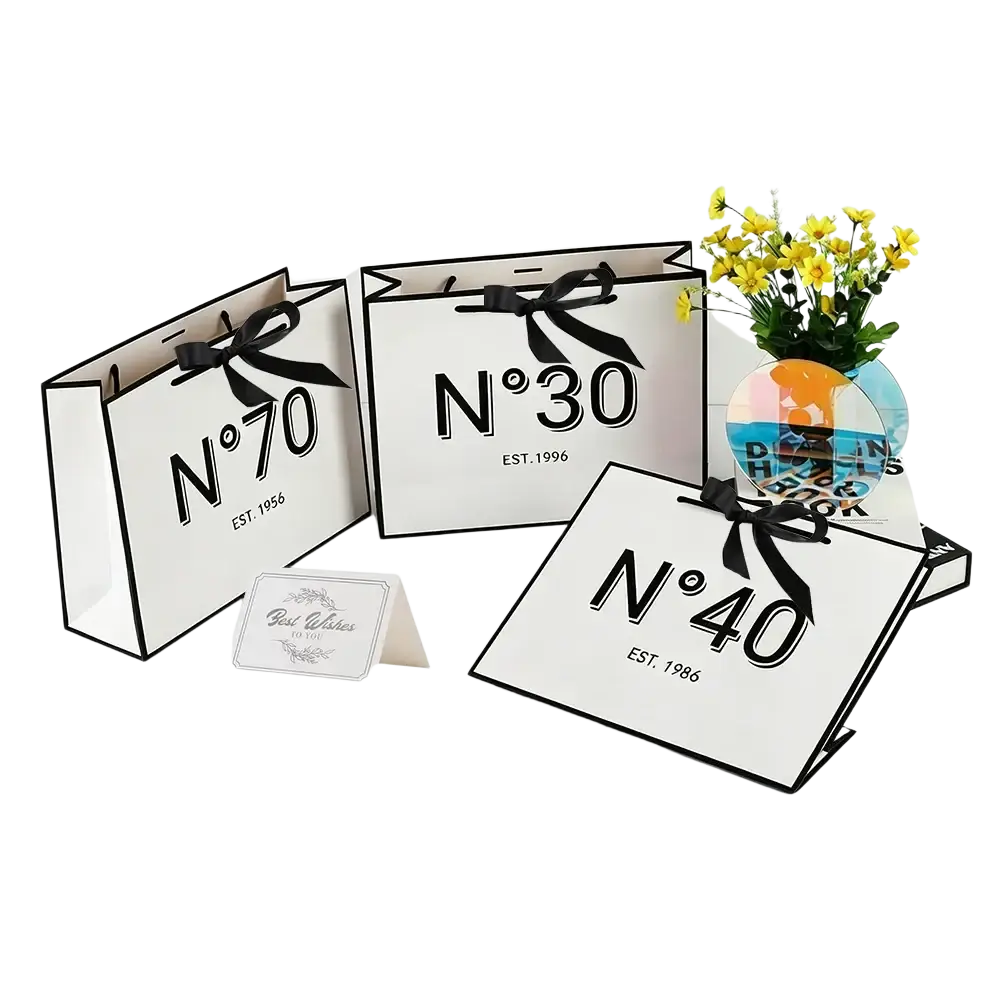 White paper shopping bags with black printed numbers and est dates tied with black ribbon bows for milestone birthdays