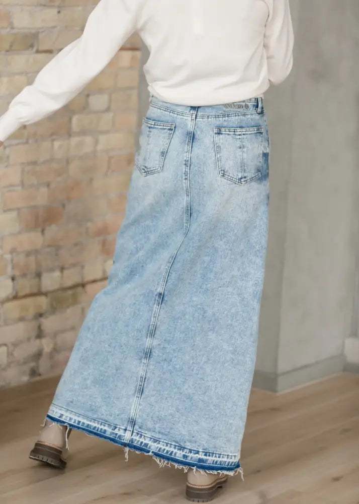 Light wash denim maxi skirt with frayed hem and back pockets shown from the back side