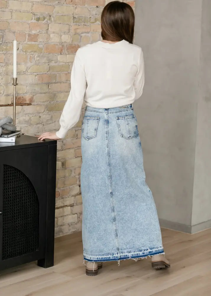 Light-wash denim maxi skirt with frayed hem and back pockets shown from the back for casual wear