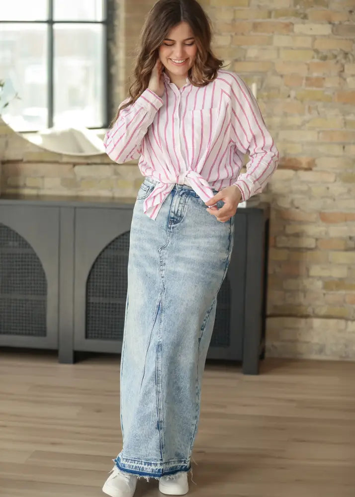 A woman wears a Mina frayed hem light wash denim maxi skirt with side seam detailing and a long frayed hem