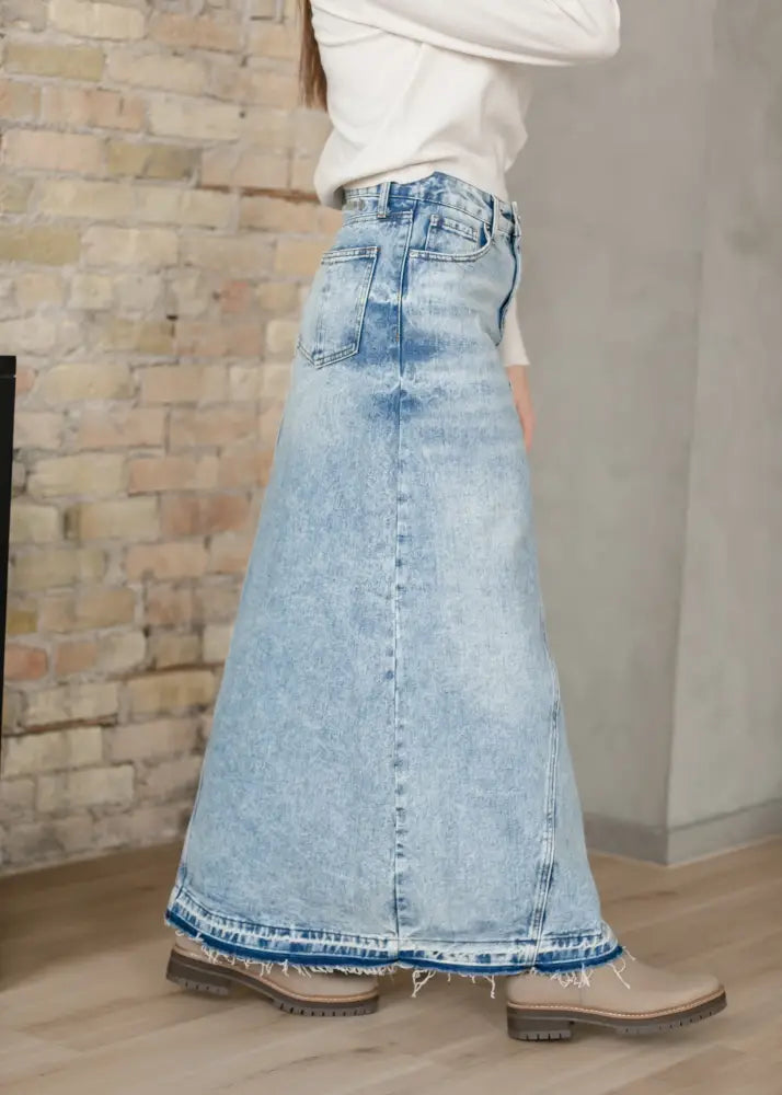 Light-wash denim maxi skirt with frayed hem and classic back pockets shown from the back in mina collection