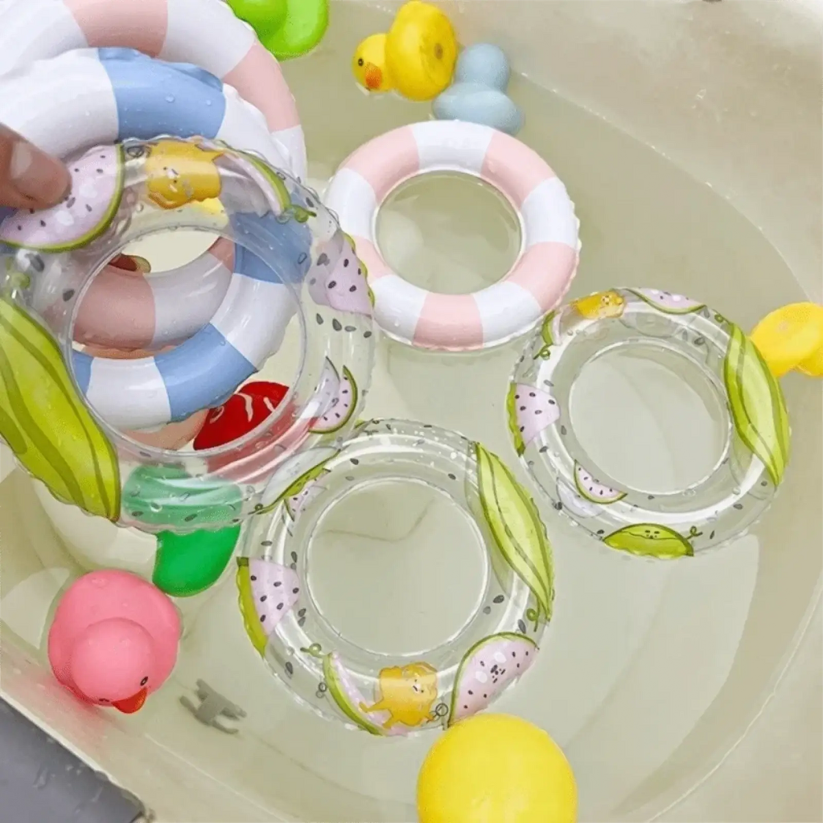 Mini turtle inflatable swim ring made of clear material with colorful fruit and cartoon duck designs floating in water