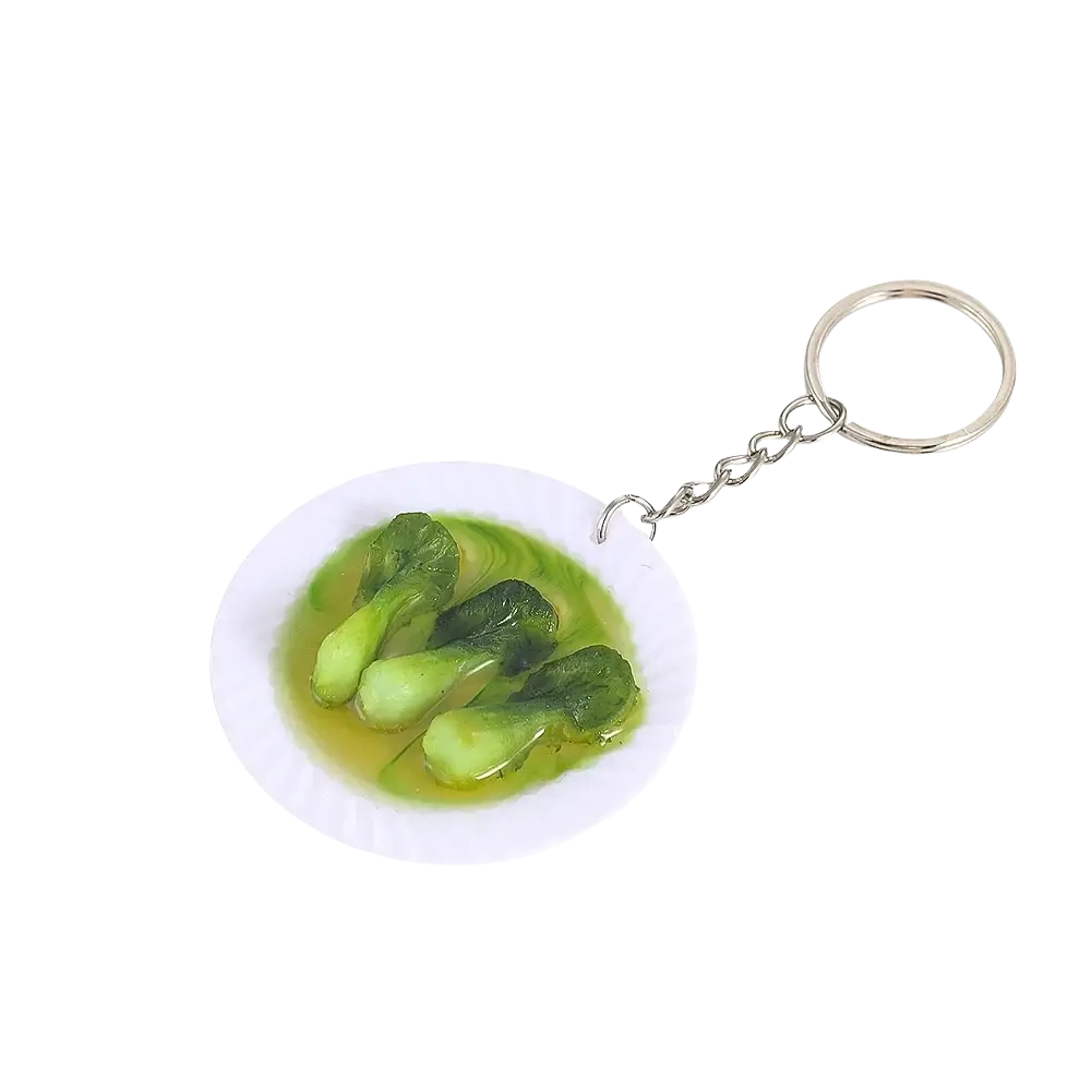 Miniature food keychain with a white plate of green bok choy leaves in light yellow broth on a silver chain ring