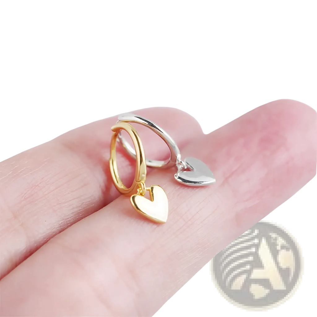 A pair of minimalist heart shaped dangle hoop earrings in gold and silver with polished metallic finish