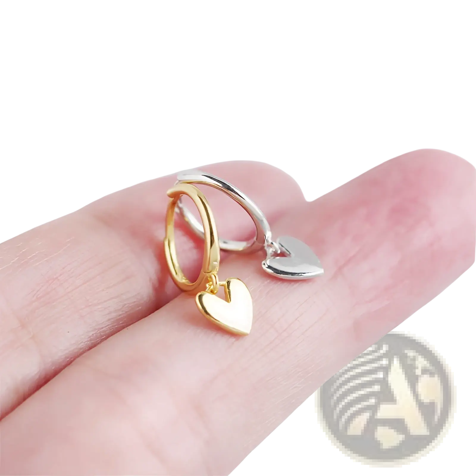 A pair of minimalist heart shaped dangle hoop earrings in gold and silver with polished metallic finish