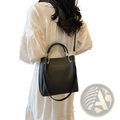 Minimalist black leather bucket bag with gold-tone hardware, top handle, and detachable strap for versatile use