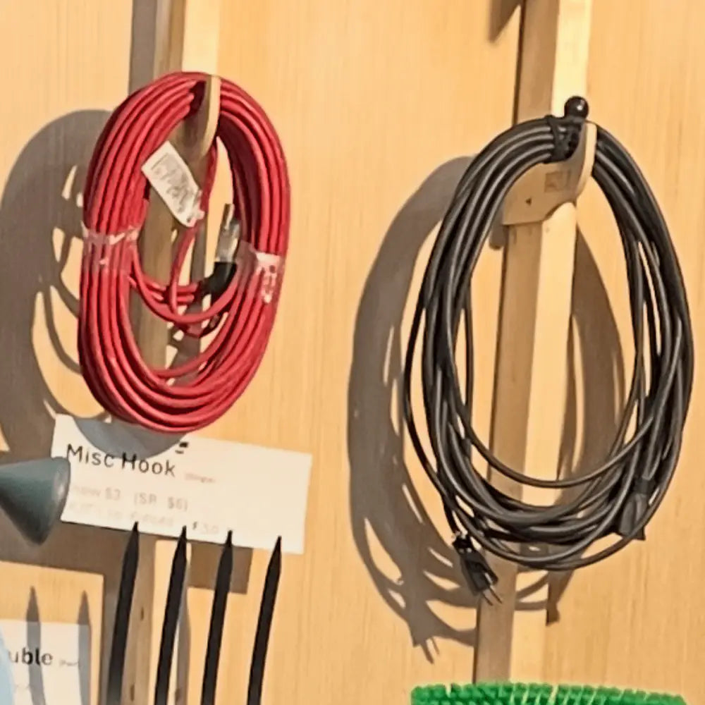 Heavy duty compact stud mounted power tool storage hooks holding red and black coiled power cords on wooden hooks