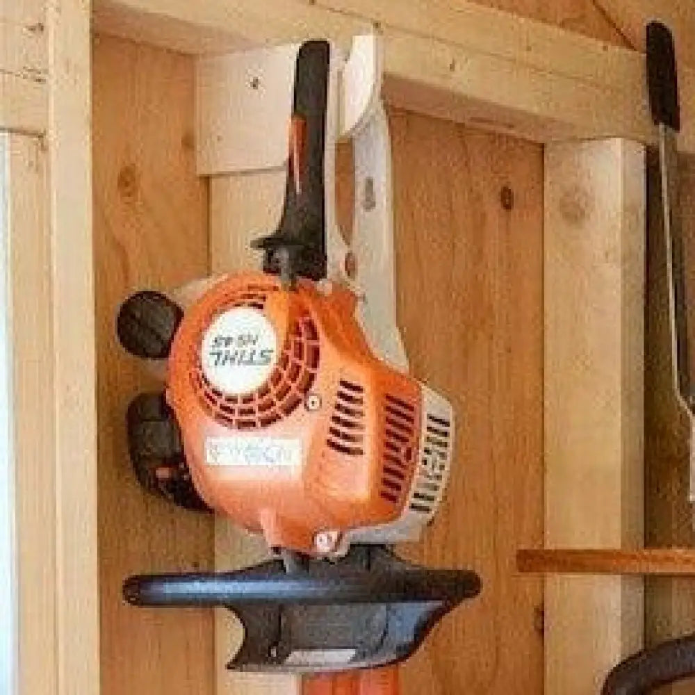 Heavy duty compact stud mounted power tool storage hook holding an orange and black stihl hedge trimmer in wood cabinet