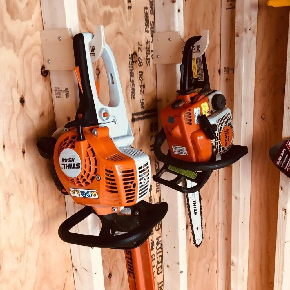 Heavy duty compact stud mounted power tool storage hook holding orange and black stihl chainsaws on wooden wall