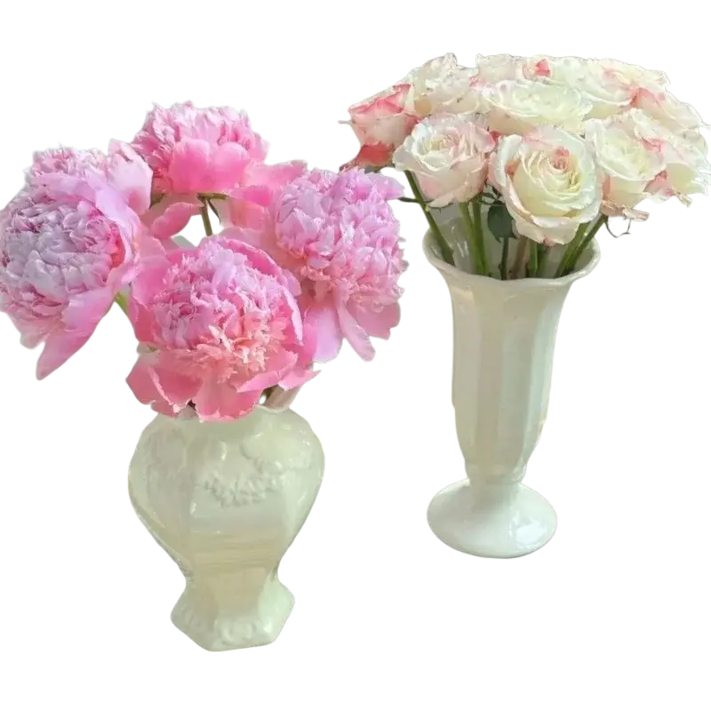 Two white french modern ceramic vases with embossed floral and fluted patterns hold pink peonies for room decor