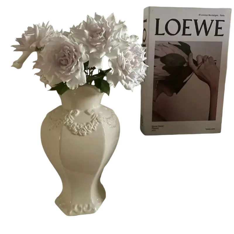 A white french modern ceramic vase with embossed floral detailing holding pale pink roses for room decor
