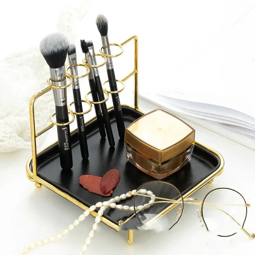 Gold-framed modern vanity cosmetics organizer with black ceramic tray and circular rings holding multiple makeup brushes