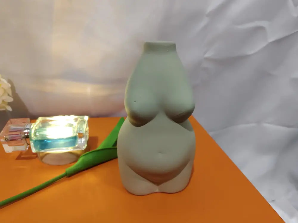 A matte sage green ceramic sculpture of a female torso with smooth curves in a modern minimalist style vase