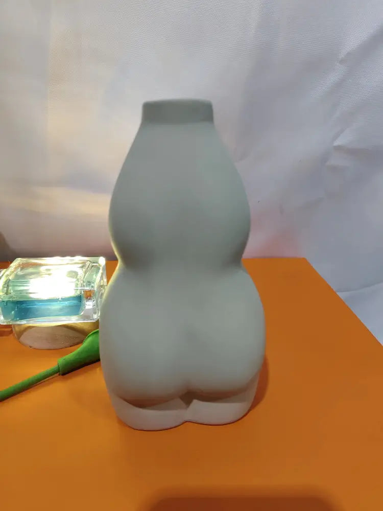 A matte gray ceramic vase shaped like a stylized female torso in modern minimalist design