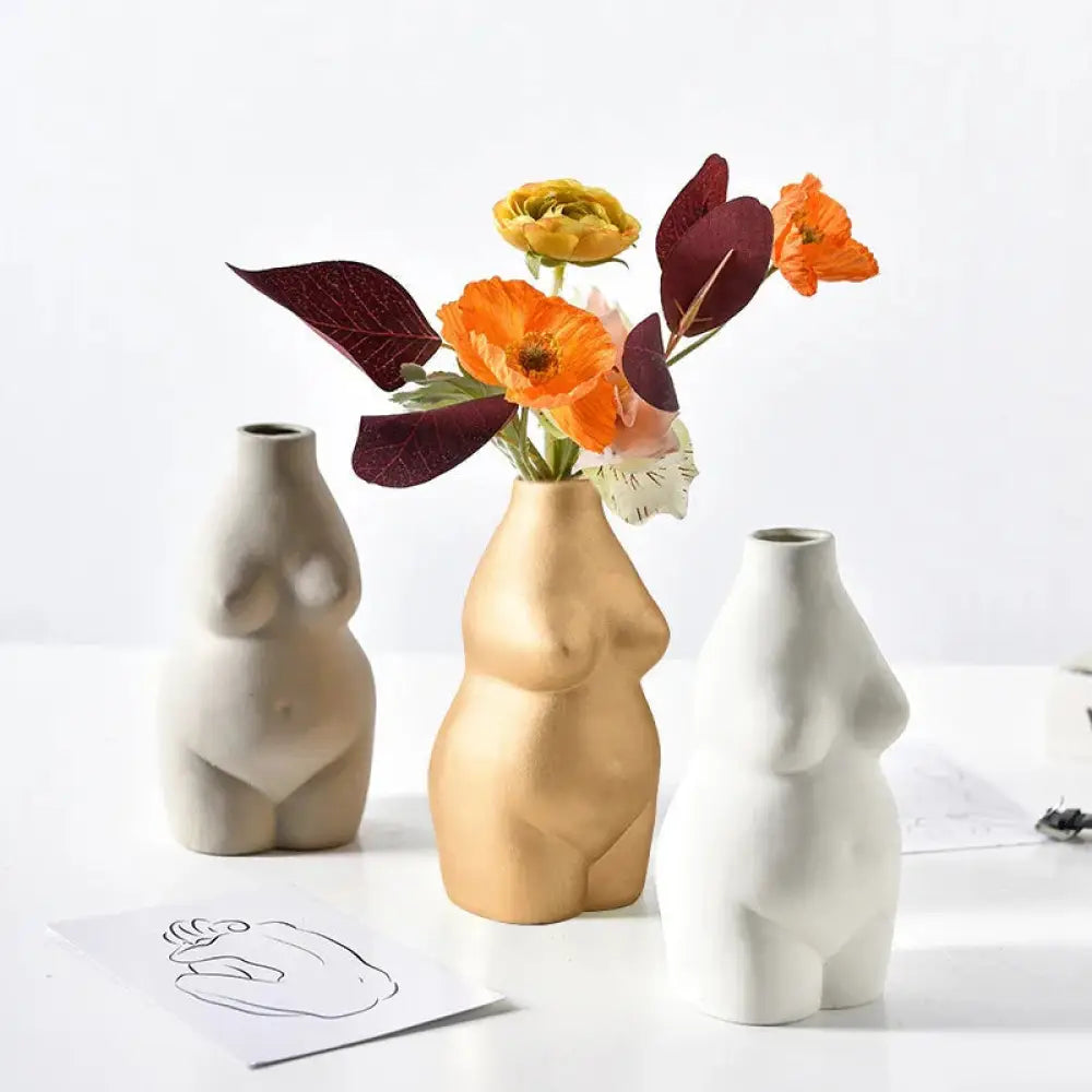 Modern minimalist female form ceramic art vase in golden with orange and yellow flowers arranged inside