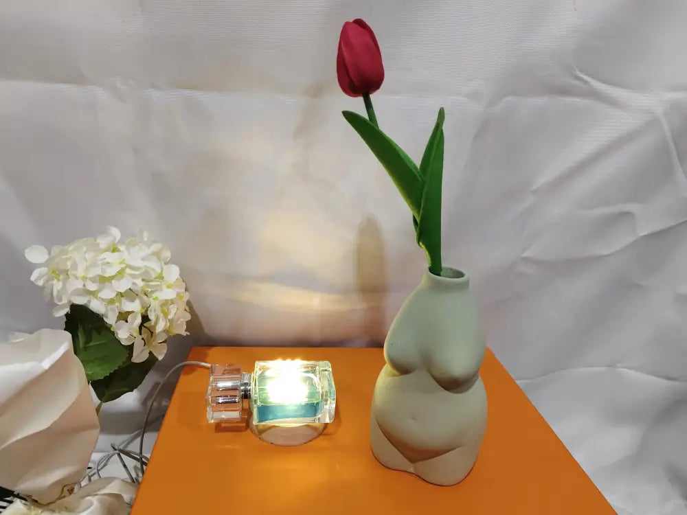 A light green ceramic vase shaped like a female torso holding a single red tulip for modern minimalist decor
