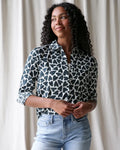 A woman wears a black and white heart-patterned cotton More Love Giraffe button-up blouse with rolled sleeves