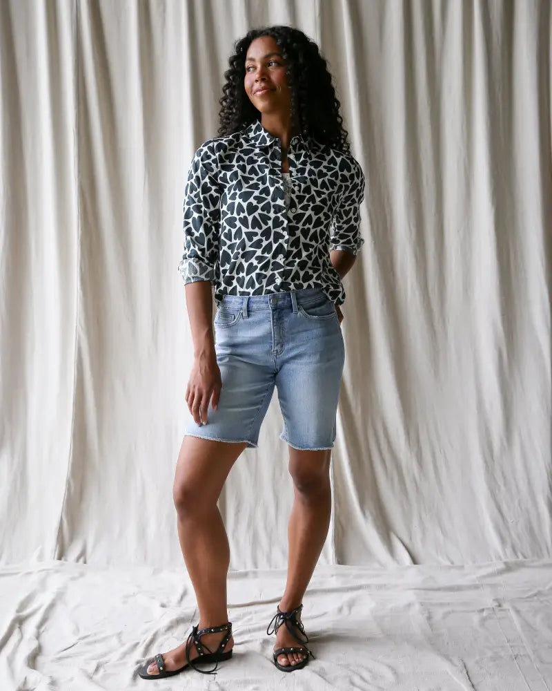 A woman wears a black and white giraffe heart print cotton button up blouse with rolled sleeves
