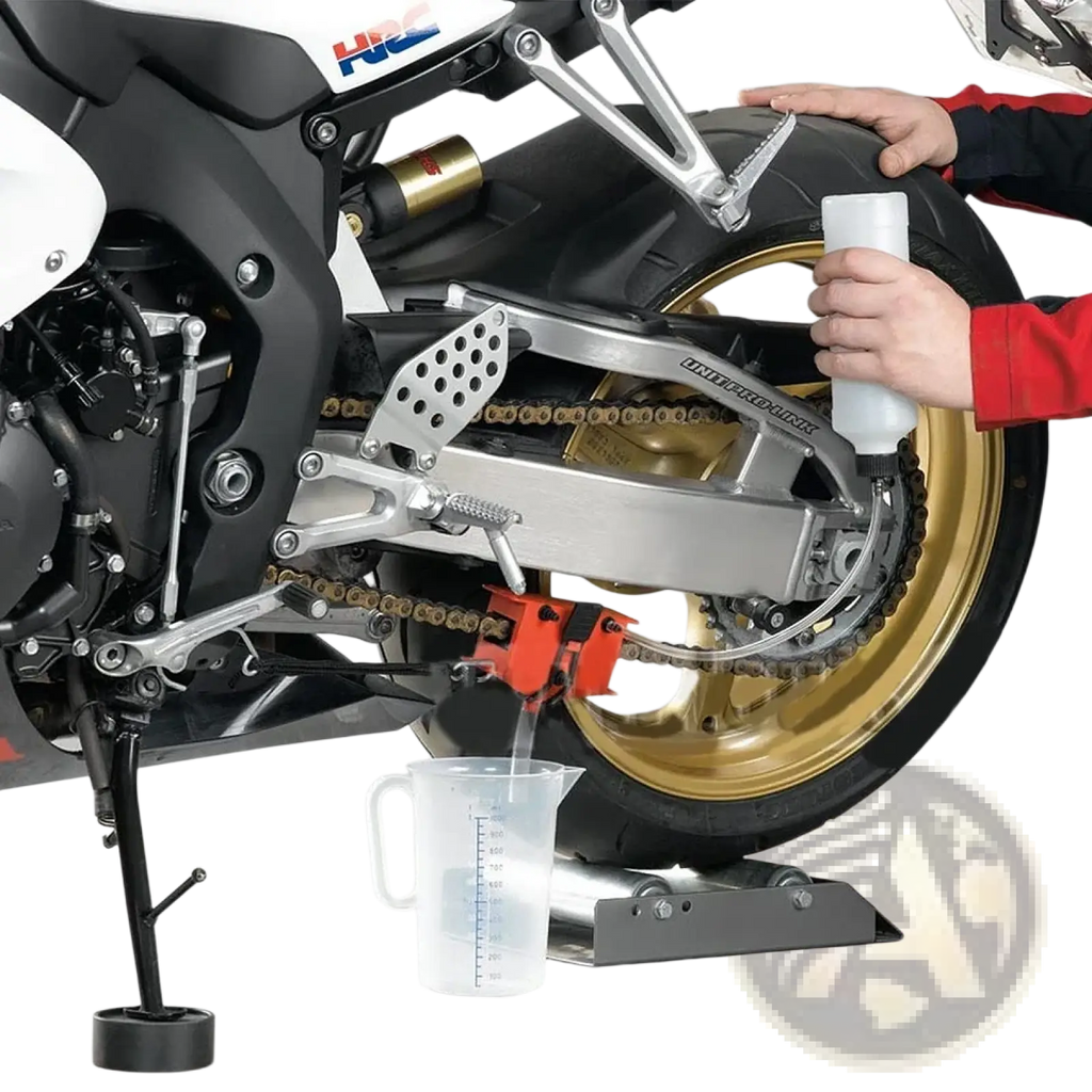 A red motorcycle chain cleaner and lube tool with a metallic handle positioned under the rear wheel