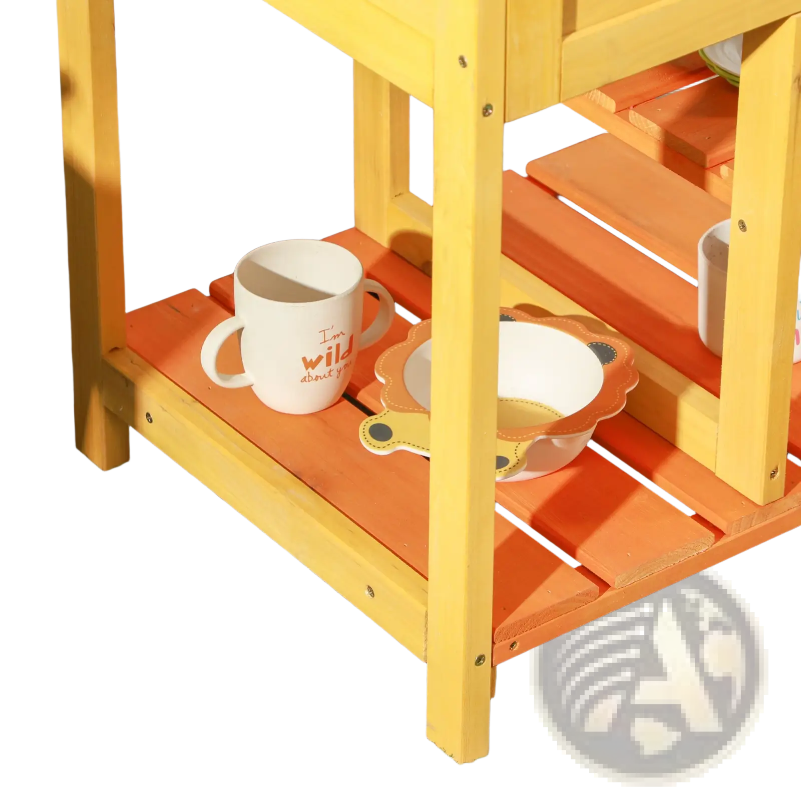 A white ceramic mug with orange text beside a lion-themed bowl on an outdoor wooden shelf in a mud kitchen playset