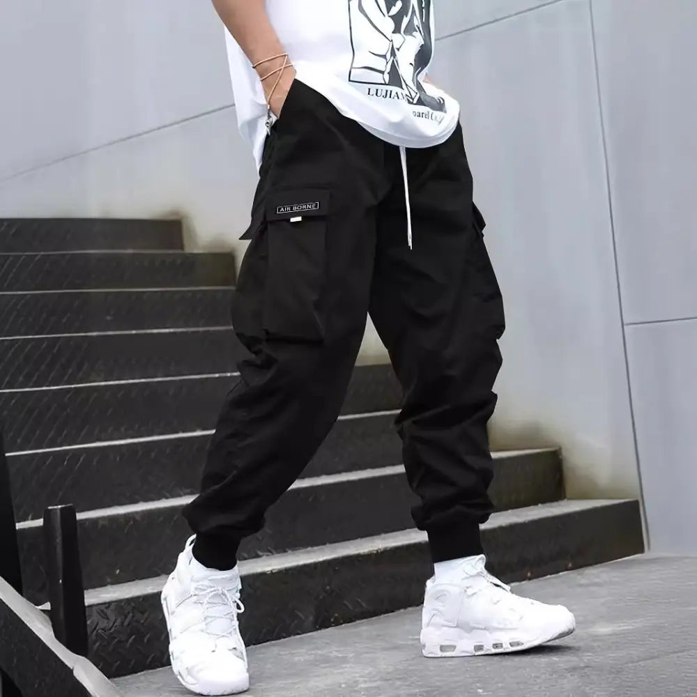 Men’s black cargo joggers with drawstring waist side pockets and subtle thigh brand patch for streetwear use