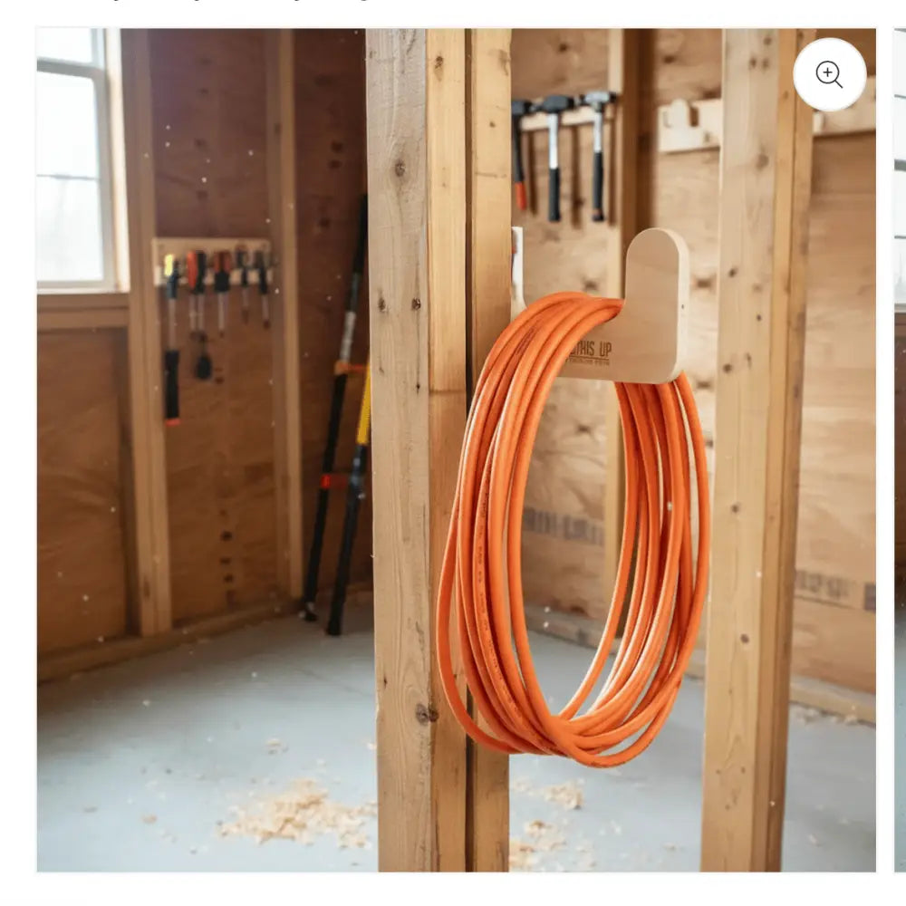 Engraved wooden stud mounted utility storage hook holding a neatly coiled orange extension cord on light wood background