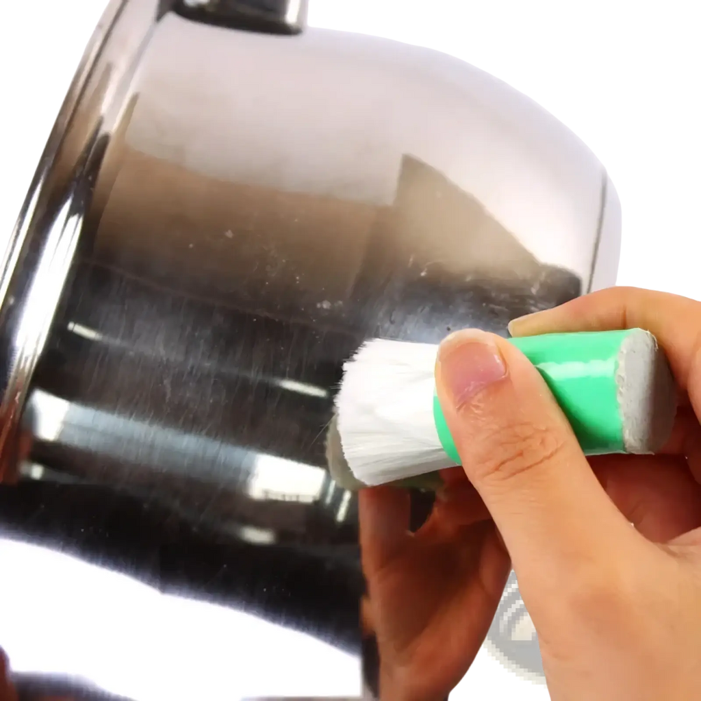 Multifunctional kitchen scrub brush with green handle and white bristles cleaning a stainless steel pot
