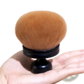 Multifunctional oversized soft powder makeup brush with plush rounded orange bristles and sleek black handle held in palm