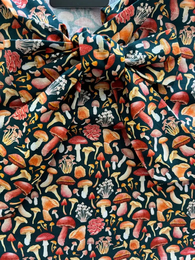 Vintage mushroom print sleeveless bow top with vibrant red orange and white fungi on dark fabric background