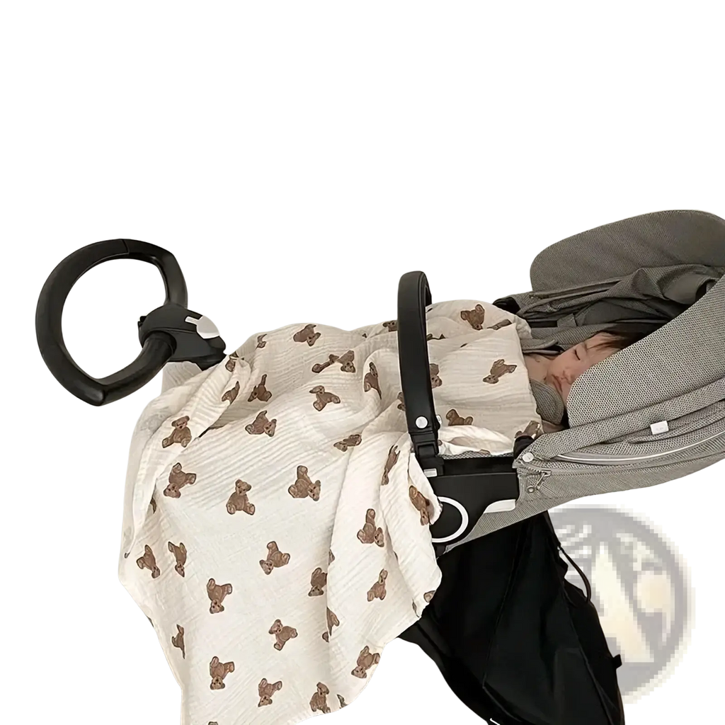 A soft off-white muslin bear print baby bath towel and swaddle blanket draped over a stroller