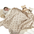 Beige muslin cotton baby swaddle blanket with subtle brown rainbow pattern and stitched edges gently wrapped around baby